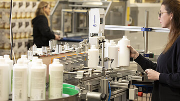 Maschine mit Flasche und Frau die diese befüllt